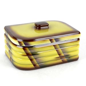 May include: A rectangular ceramic container with a lid. The container is yellow with brown accents and a brown knob on top. The sides have a ribbed design. The overall shape is square with rounded corners.