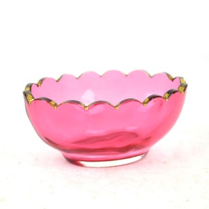 Può includere: Una piccola ciotola di vetro rosa con bordo ondulato e bordo dorato.
