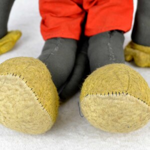 May include: A vintage plush toy Mickey Mouse with black fur, red shorts, and yellow felt shoes. The toy has a stitched seam around the edges of the shoes.