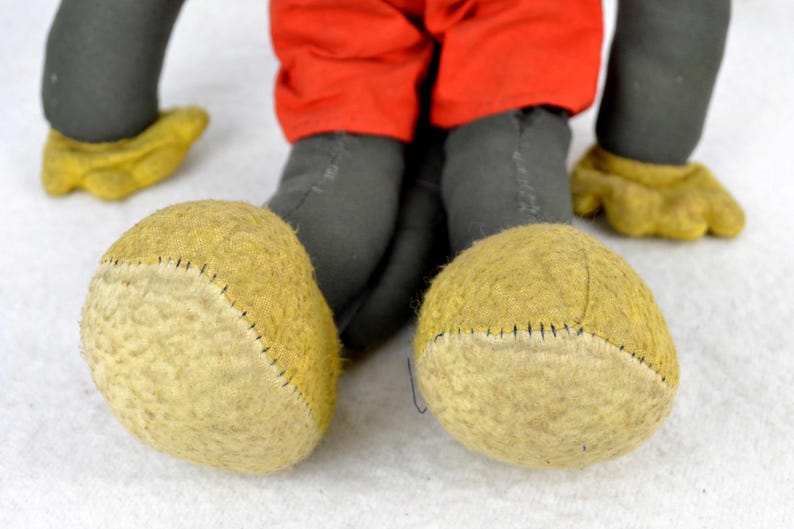 May include: A vintage plush toy Mickey Mouse with black fur, red shorts, and yellow felt shoes. The toy has a stitched seam around the edges of the shoes.