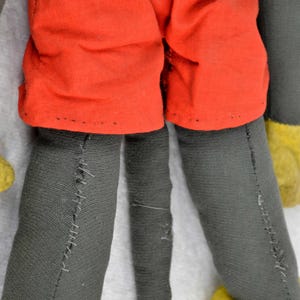 May include: A vintage plush toy of Mickey Mouse. The toy is wearing red shorts and has a black tail. The toy is made of grey fabric and has yellow shoes.