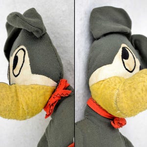 May include: A vintage plush toy dog with a grey body, yellow beak, and red scarf. The dog has large, white eyes with black pupils.