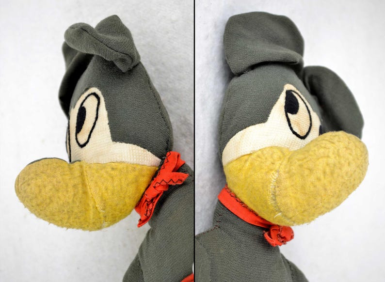May include: A vintage plush toy dog with a grey body, yellow beak, and red scarf. The dog has large, white eyes with black pupils.