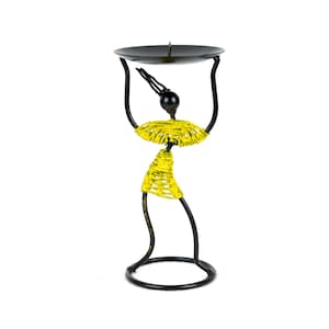 May include: A decorative black metal candle holder in the shape of a stylized figure. The figure has a yellow beaded skirt and a black head, holding a round black plate. The candle holder is designed to hold a single candle.