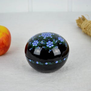 以下が含まれることがあります： 青い花と緑の葉で飾られた、黒い丸い小箱。