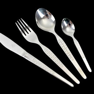 May include: A set of four stainless steel utensils: a knife, fork, and two spoons. Each piece has a decorative pattern on the handle. The silverware is arranged diagonally against a black background.