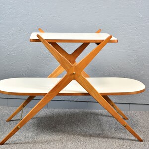 May include: A two-tiered wooden table with a white top. The table has a unique X-shaped design and features brass accents.