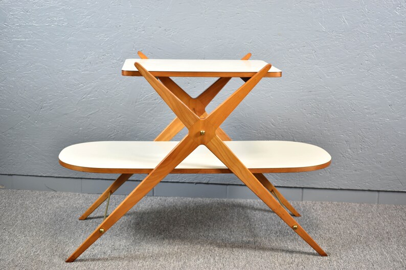 May include: A two-tiered wooden table with a white top. The table has a unique X-shaped design and features brass accents.