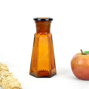 Könnte beinhalten: Eine braune Glasflasche mit schwarzem Deckel und einem strukturierten Design. Die Flasche ist leer und hat einen kleinen Buchstaben "Z" auf der Seite eingeätzt.