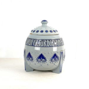 Può includere: Un vaso di ceramica con coperchio, decorato con motivi floreali blu e bianchi e il testo "Schlufer für den Wonnemond".