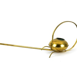 May include: A gold-colored metal watering can with a long spout and a circular handle. The watering can has a rounded body and a decorative design.