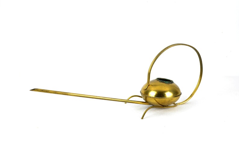 May include: A gold-colored metal watering can with a long spout and a circular handle. The watering can has a rounded body and a decorative design.