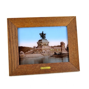 May include: A framed photograph of a monument with a statue of a person on horseback. The monument is made of stone and has a large archway. The photograph is in a wooden frame with a gold plaque that says "Deutsches Reich".