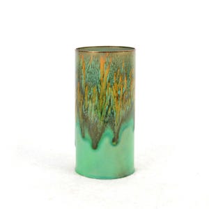 Op de afbeelding: Een cilindrische vaas met een groene en oranje glazuur. De glazuur heeft een druppel effect, waardoor een unieke en artistieke look ontstaat.