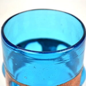 May include: A blue glass drinking glass with a copper band around the middle. The glass has a rounded bottom and a slightly flared top.