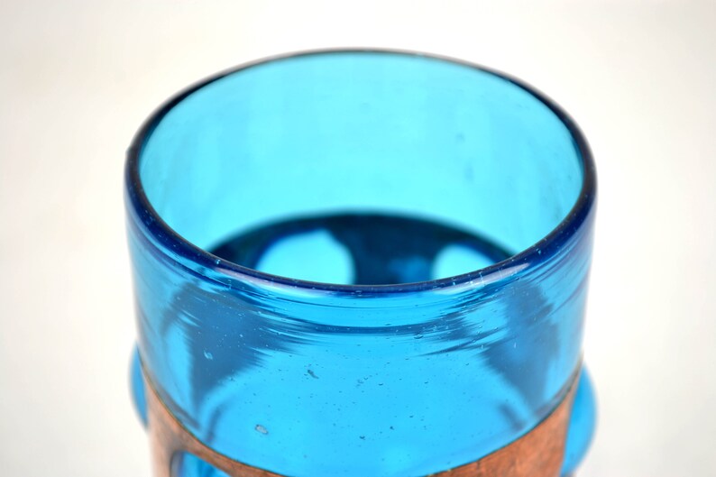 May include: A blue glass drinking glass with a copper band around the middle. The glass has a rounded bottom and a slightly flared top.