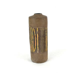 Könnte beinhalten: Eine braune Keramikvase mit einem geometrischen Muster in Gelb und Orange. Die Vase ist zylindrisch geformt und hat eine glatte, matte Oberfläche.