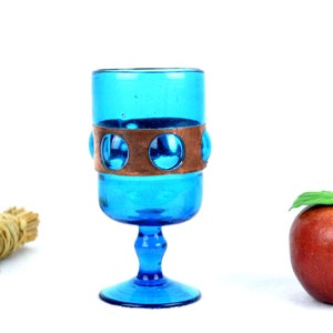 May include: A blue glass goblet with a copper band and a round base. The goblet is filled with a clear liquid.