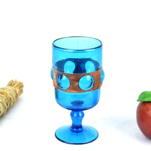 May include: A blue glass goblet with a copper band around the middle. The goblet has a round base and a stem.