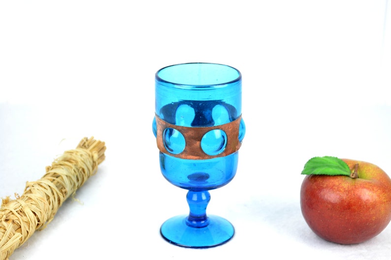 May include: A blue glass goblet with a copper band around the middle. The goblet has a round base and a stem.