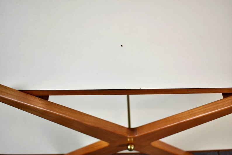 May include: A white table top with a wooden base. The base is made of four pieces of wood that are crossed in an X shape. The table is made of wood and has a white finish.