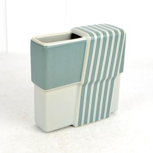 Könnte beinhalten: Eine Keramikvase mit geometrischem Design. Die Vase ist aus weißer und hellblauer Keramik gefertigt und hat auf einer Seite ein gestreiftes Muster.