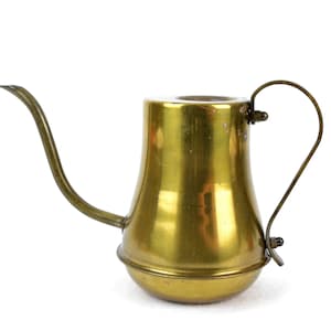 Könnte beinhalten: Kleiner, antiker Gießkanne aus Messing mit langem, gebogenem Ausguss und Schlaufengriff. Die Kanne hat einen abgerundeten Boden und einen zylindrischen Körper mit glänzendem, goldenem Finish. Für die zarte Pflanzenpflege.