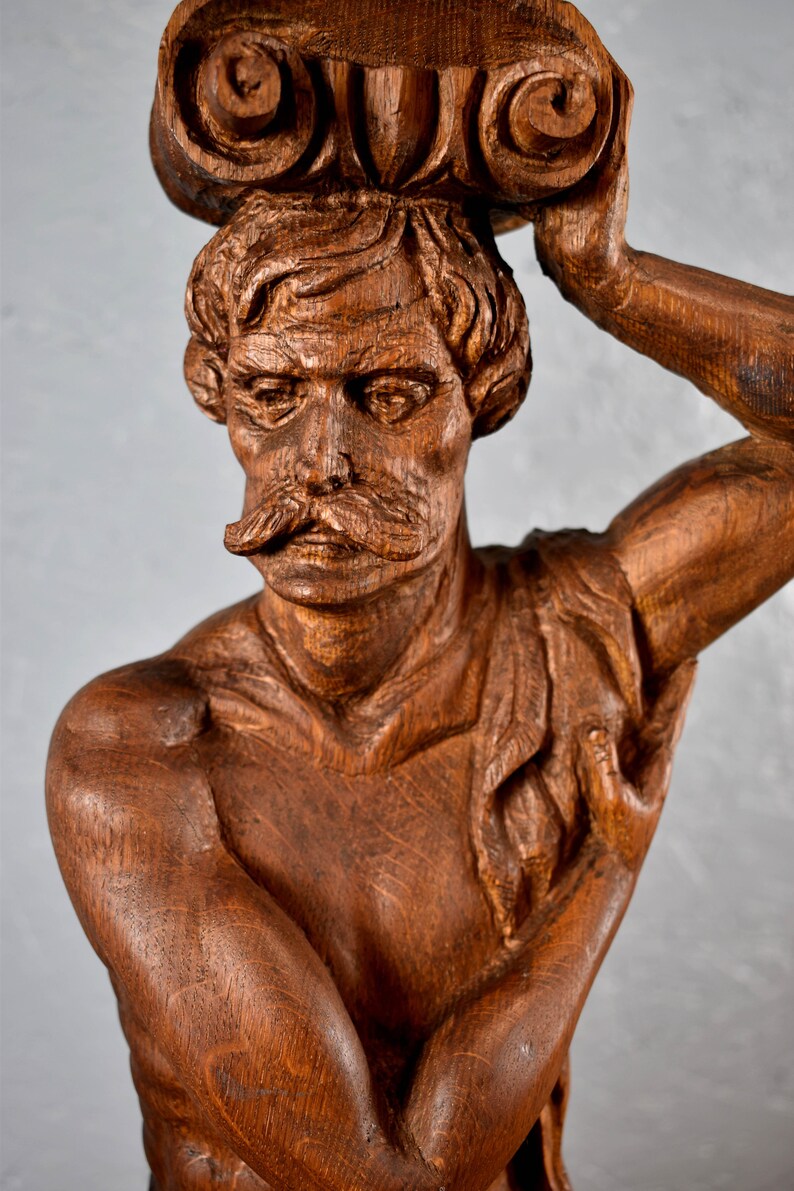 Puede incluir: Una escultura de madera detallada de un busto de hombre con un rollo en la cabeza. La escultura est&aacute; tallada en madera marr&oacute;n oscura y tiene un aspecto realista.