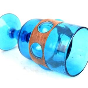 May include: A blue glass goblet with a copper band around the middle. The band has a series of circular cutouts.