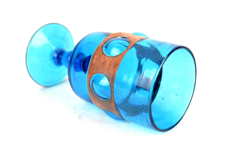May include: A blue glass goblet with a copper band around the middle. The band has a series of circular cutouts.