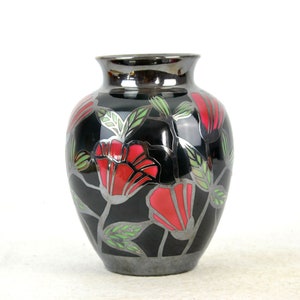 Op de afbeelding: Een zwarte keramische vaas met een zilveren metallic glazuur en een rood en groen bloemenontwerp.