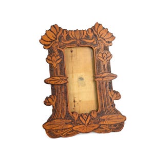 May include: A decorative wooden picture frame with an intricate floral design. The frame is a warm brown color and features carved details of flowers and leaves. The frame is empty, with a light-colored backing visible.