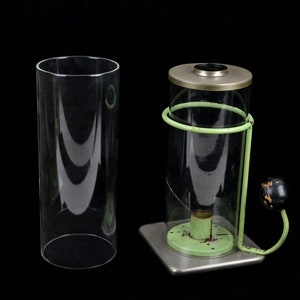 May include: A clear glass cylinder and a vintage candle holder. The candle holder has a clear glass chimney, a green metal frame, and a black knob. The base is square and silver-colored.