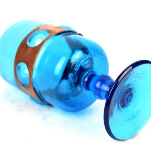 May include: A blue glass goblet with a copper band around the middle. The goblet has a wide base and a round bowl.