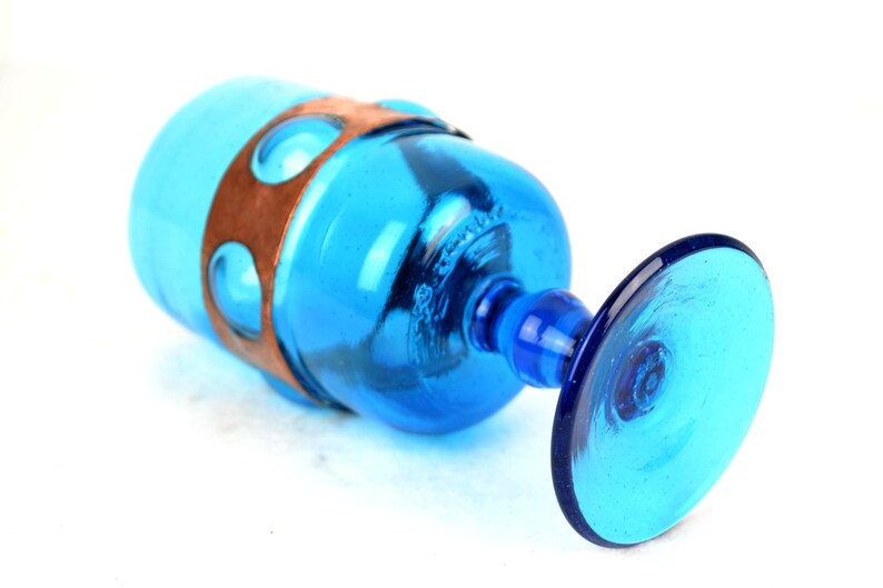 May include: A blue glass goblet with a copper band around the middle. The goblet has a wide base and a round bowl.