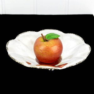 May include: A red apple with a green leaf sits in a silver, scalloped serving dish on a black background.