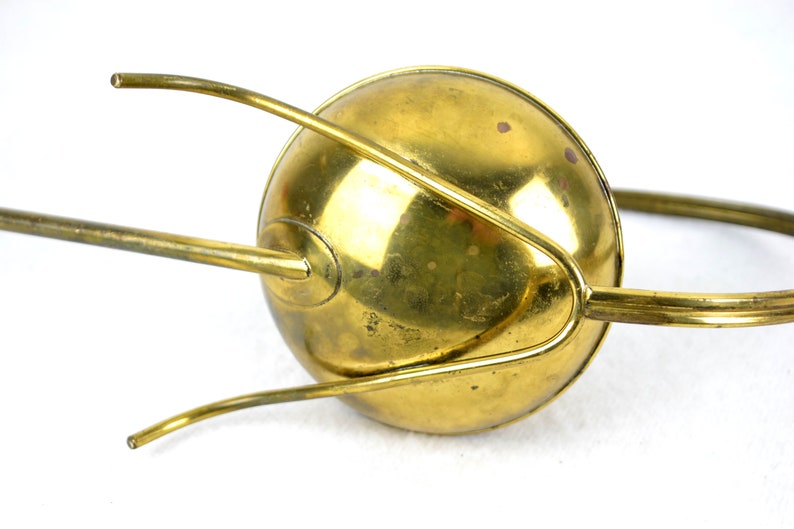 May include: A brass watering can with a long spout and a handle. The can has a rounded shape and a shiny finish.