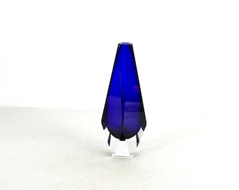 Könnte beinhalten: Eine kobaltblaue Glasvase mit geometrischem Design. Die Vase hat einen klaren Glasfuß.