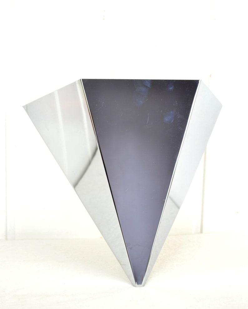 May include: A silver, triangular-shaped vase with a shiny, reflective surface.