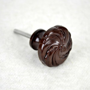 May include: A dark brown wooden cabinet knob with a swirl design. The knob has a silver screw.