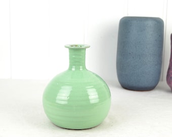 May include: A light green ceramic vase with a round body and a narrow neck. The vase has a smooth, glossy finish.