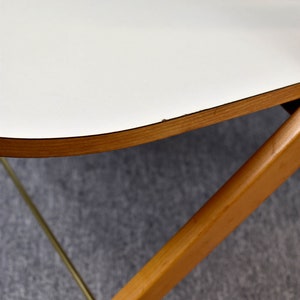 May include: A white table top with a rounded edge and a natural wood trim. The table is supported by a wooden frame with a brass accent.