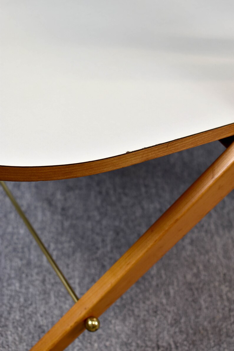 May include: A white table top with a rounded edge and a natural wood trim. The table is supported by a wooden frame with a brass accent.