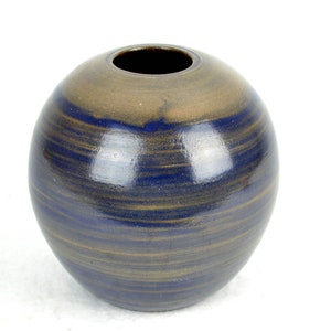 Puede incluir: Un jarrón redondo de cerámica con un esmalte azul y marrón. El jarrón tiene un acabado liso y brillante y una abertura ancha.