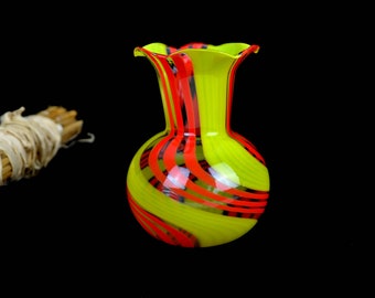 May include: A yellow glass vase with red and black stripes. The vase has a rounded body and a flared opening.