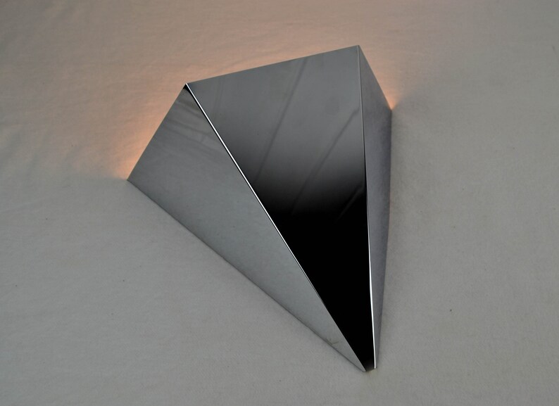 May include: A shiny, silver, triangular-shaped wall sconce with a modern design.