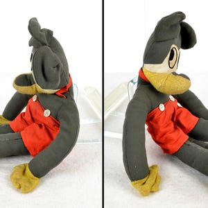 May include: A vintage plush Mickey Mouse toy with black fur, red shorts, and yellow shoes. The toy is sitting with its legs outstretched and its head turned to the side.
