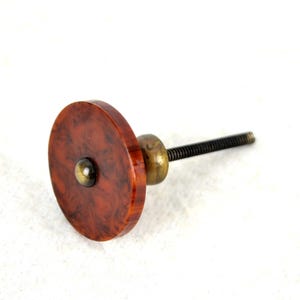 May include: A brown and red marbled round cabinet knob with a brass screw and a metal accent.