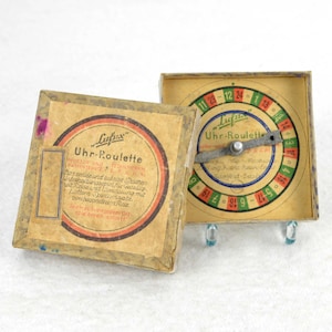 May include: A vintage wooden box game called "Uhr-Roulette" by Lufix. The box has a colorful roulette wheel with numbers and a metal pointer. The box is open and the roulette wheel is visible.