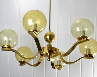 May include: A gold-toned chandelier with five frosted glass globes. The chandelier has a curved, modern design.